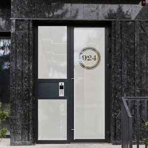 May include: A black door with a glass panel and a gold circle with the number 924 on it. The door is on a building with black granite walls and a set of stairs leading up to it.