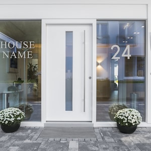 May include: A white front door with a glass panel and a silver door handle. The door is flanked by two windows with the text "HOUSE NAME" on the left window and the number "24" on the right window. There are two potted plants with white flowers in front of the windows.