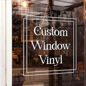 May include: A white shopfront window with a sign that reads "Custom Window Vinyl" in a white sans-serif font. The sign is framed with a double white border.