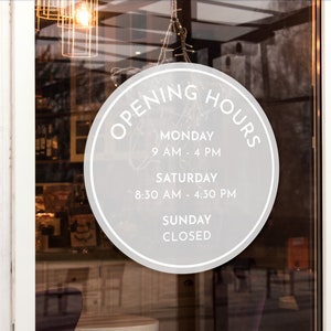 May include: A white circle sticker on a glass door with the text "OPENING HOURS" in a black circle. The sticker lists the store's hours of operation: Monday 9 AM to 4 PM, Saturday 8:30 AM to 4:30 PM, and Sunday Closed.