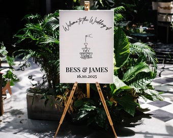 May include: A white sign with black text and a graphic of a champagne tower on an easel. The sign reads "Welcome to the Wedding of Bess & James 16.10.2025".