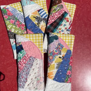 May include: A collection of six handmade quilted pot holders. Each pot holder features a unique patchwork design with various floral, striped, and patterned fabrics. The pot holders have a yellow and white gingham backing and white quilted edges.