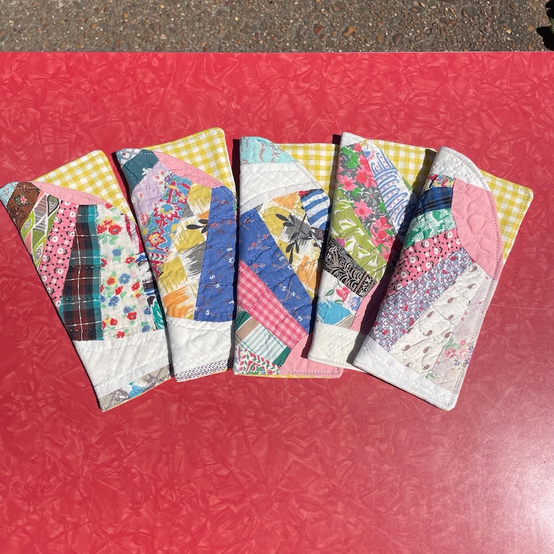 May include: Five handmade quilted coasters with a variety of colorful fabric patterns. Each coaster features a unique patchwork design with floral, plaid, and geometric prints. The coasters have a white border and a yellow gingham backing.