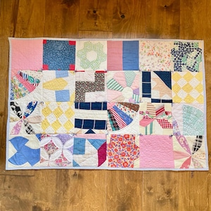 May include: A patchwork quilt with a variety of colorful fabrics and patterns. The quilt is made up of squares and rectangles, and the fabrics include floral prints, stripes, and solids. The quilt is edged with a blue and white trim.