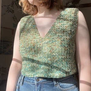 May include: A sleeveless crochet top in a green, brown, and white speckled pattern. The top has a v-neck and is cropped.