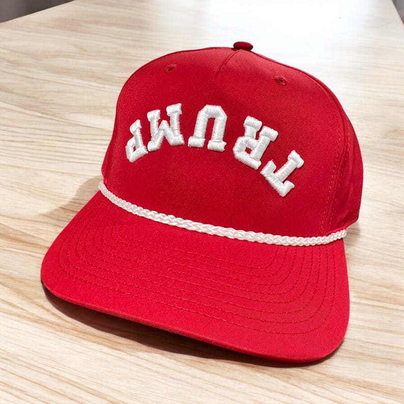 May include: Red baseball cap with a white rope trim and the word "TRUMP" embroidered in white on the front.