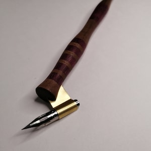 May include: A wooden calligraphy pen with a purple and brown striped handle and a gold metal nib.