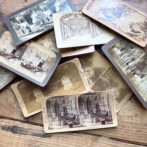 Op de afbeelding: Een verzameling vintage stereoscopische kaarten met sepia-kleurige afbeeldingen van architectuur, landschappen en mensen. De kaarten zijn gerangschikt op een rustiek houten oppervlak, wat hun verouderde uiterlijk en historische charme benadrukt.