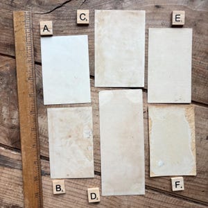 May include: A collection of vintage ephemera, including aged paper rectangles and wooden Scrabble tiles with letters. A wooden ruler is positioned along the left side. The items are arranged on a rustic wooden surface, creating a nostalgic aesthetic.