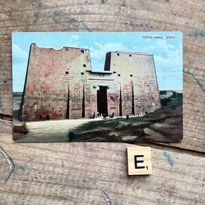 May include: Vintage postcard depicting the Temple Gates of Edfu, Egypt. The postcard features a detailed illustration of the ancient stone structure with intricate carvings and a blue sky background.