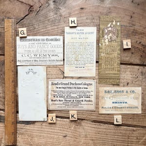 May include: A collection of vintage ephemera, including advertisements and a calendar, arranged on a wooden surface. The items feature text and graphics, with a ruler along the left side. The color palette is muted, with sepia tones and aged paper textures.