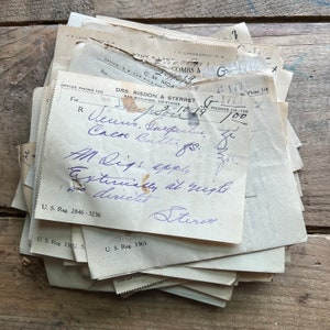 May include: A close-up of a stack of old, white paper receipts with handwritten notes in purple ink. The text on the top receipt reads "DRS. RISDON & STERRET AXA BUILDING, UPSTAIRS NEW. PHONES 114-130" and "Venus, Aerosol, Cacao, Butter, for it, M. Dig: apply, Externally at night, direct, Sterox".