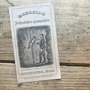 May include: Black and white illustration of a man operating a rock drill in a mine shaft. The illustration is from a vintage advertisement for the Burleigh Rock Drill Company in Fitchburg, Massachusetts.