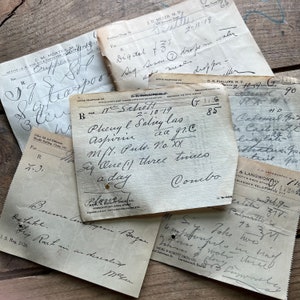 May include: Close-up of several vintage prescription slips with handwritten text. The slips are on a wooden surface. The text includes medical terms, dosages, and dates. One slip reads "Phenyl Salicy las aa gr.c Aspirin Mft. Puls. No. XX Siq One (1) three times a day Coucbo".