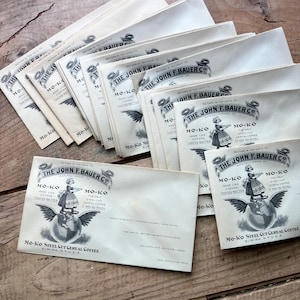 May include: A collection of vintage Mo-Ko Steel Cut Cereal Coffee packets. Each packet features the text "The John F. Bauer Co." and an illustration of a woman atop a globe with wings. The packets are cream-colored with black text.