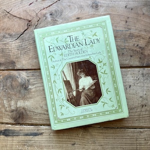 May include: A hardcover book titled "The Edwardian Lady" with a light green cover and decorative floral elements. The book features a sepia-toned image of a woman painting. The title and author's name are printed in a classic serif font.