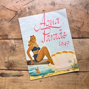 May include: Vintage "Aqua Parade of 1949" magazine cover. The cover features a woman in a blue swimsuit, sitting near a seashell illustration. The title is in pink script, with the price of 25 cents in the lower right corner.