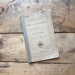 May include: A vintage tan paper-bound booklet titled Erection and Dedication of the Soldiers and Sailors Monument in the Army and Navy Lot, Mount Hope Cemetery, City of Boston, printed in 1867, featuring black text and circular ink stamps.