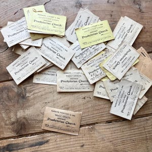 May include: A collection of vintage Presbyterian Church offering cards, scattered on a rustic wooden surface. The cards, in various shades of cream and yellow, feature handwritten text, dates, and the church name. The overall aesthetic is aged and historical.