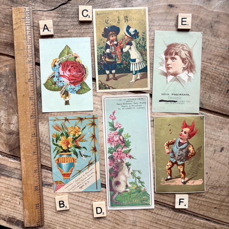 May include: A collection of antique postcards, featuring floral designs, children, and illustrations. The cards showcase a variety of styles, including a rose with a banner, a vase of flowers, and a child's portrait. The cards are arranged on a wooden surface.
