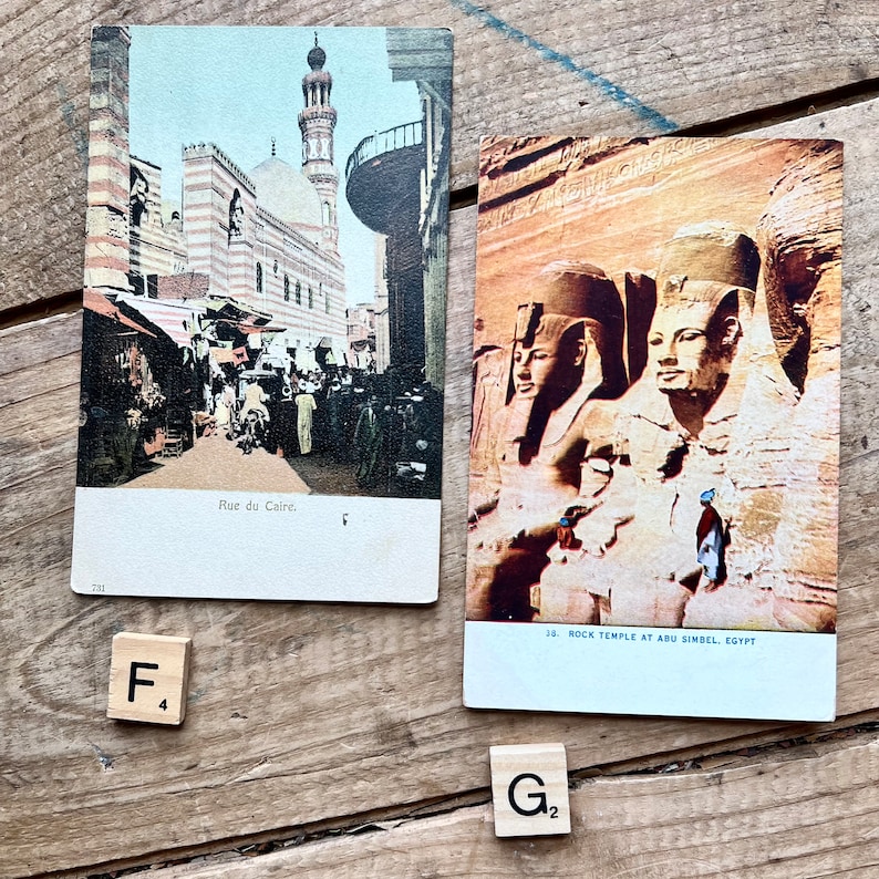 May include: Two vintage postcards depicting scenes from Egypt. The first postcard shows a street scene in Cairo with a mosque in the background. The second postcard shows the rock temple at Abu Simbel with the four colossal statues of Ramses II.