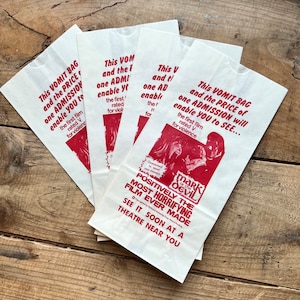 May include: Four white paper bags with red text advertising the movie "Mark of the Devil". The text reads "This vomit bag and the price of one admission will enable you to see... Positively the most horrifying film ever made. See it soon at a theatre near you."