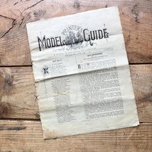 May include: An aged, off-white paper page titled Model Printer's Guide, A Journal of Typography and Literature, Philadelphia, June 1876. The document features black printed text, including the stories Katy Did It and Hans Peppenheimer.