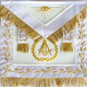 May include: White Masonic apron with gold embroidery. The apron features a compass and square, an all-seeing eye, and a wreath of leaves. The apron has gold fringe around the edges.
