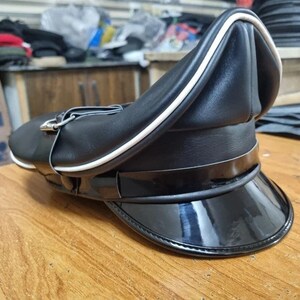 Puede incluir: Una gorra de cuero negro con una banda blanca alrededor de la corona y una visera de cuero patentado negro.