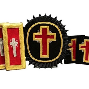 Może przedstawiać: Zestaw haftowanych naszywek z czerwonym krzyżem z pozłacanymi obramowaniami na czarnym tle. Naszywki są w różnych rozmiarach i kształtach, w tym duża okrągła naszywka, dwie prostokątne naszywki i dwie mniejsze kwadratowe naszywki.