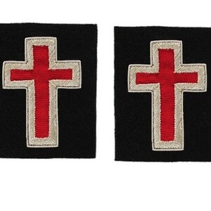 Może przedstawiać: Dwa czarne łatki z tkaniny z wyszytym czerwonym krzyżem w środku. Krzyż jest obwiedziony srebrną nicią.