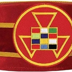 May include: A red velvet Masonic hat with a gold trim and a circular emblem featuring a red triangle, a square with nine colored squares, and a gold border.