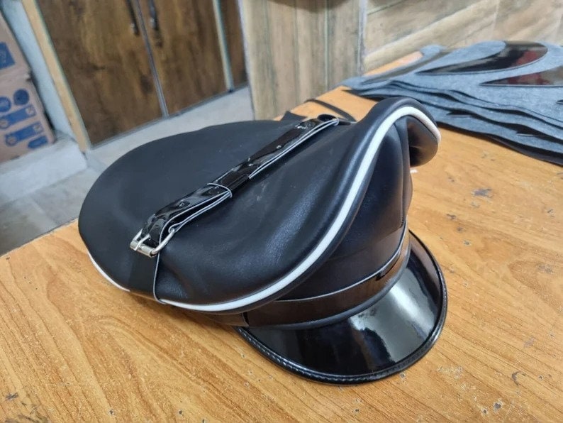 Puede incluir: Una gorra de cuero negro con una banda blanca alrededor del borde y una correa de cuero negro con una hebilla plateada.