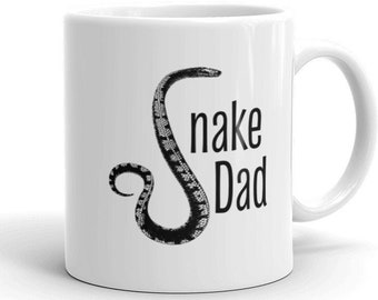 May include: White ceramic mug with a black and white illustration of a snake and the text "Snake Dad".
