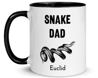 May include: White ceramic mug with a black rim and handle. The mug has a black and white illustration of a snake and the text "Snake Dad Euclid".
