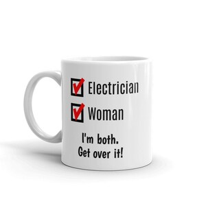 May include: White ceramic mug with a black and white checklist that says "Electrician" and "Woman" with checkmarks next to each. The text below the checklist says "I'm both. Get over it!"