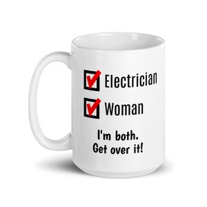 May include: White ceramic mug with a black and red design. The design features two checkboxes with checkmarks. The text in the checkboxes reads "Electrician" and "Woman". Below the checkboxes is the text "I'm both. Get over it!"
