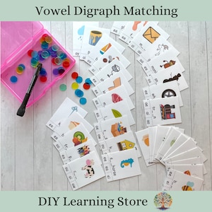 May include: A learning activity set with the text "Vowel Digraph Matching." The set includes flashcards with illustrations and letter combinations, a pink container, a black marker, and colorful translucent counters. The DIY Learning Store logo is at the bottom.