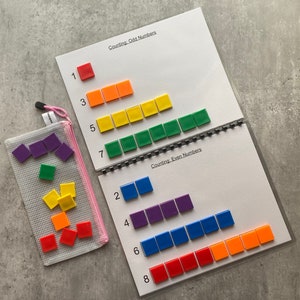 May include: A learning activity set for counting odd and even numbers. The set includes a spiral-bound booklet with number lines and colorful square tiles. A pink mesh bag holds additional tiles. The booklet reads "Counting: Odd Numbers" and "Counting: Even Numbers".