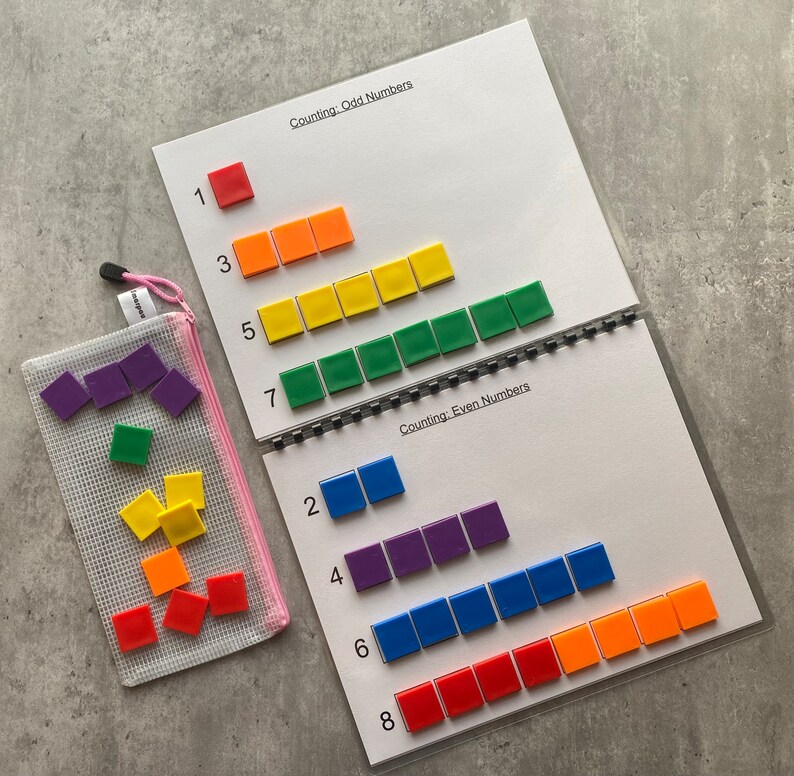 May include: A learning activity set for counting odd and even numbers. The set includes a spiral-bound booklet with number lines and colorful square tiles. A pink mesh bag holds additional tiles. The booklet reads "Counting: Odd Numbers" and "Counting: Even Numbers".
