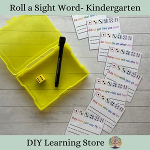May include: A yellow plastic container with a die and a black marker, alongside sight word cards for kindergarten. The cards feature sentences with spaces for writing and dice illustrations. The text "Roll a Sight Word- Kindergarten" is visible.