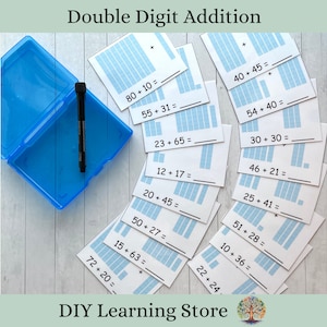 May include: A set of blue and white flashcards with double-digit addition problems. Each card has a grid to help visualize the addition. The cards are in a blue plastic container with a black marker.