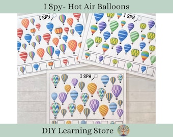 May include: Three printable "I Spy" game cards featuring hot air balloons in various colours and patterns. Each card has a magnifying glass icon and the text "I Spy".