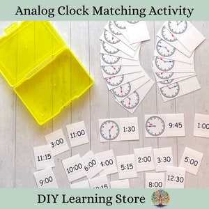 May include: A set of analog clock cards with matching time cards. The cards are white with black numbers and hands. The time cards are white with black numbers. The cards are arranged in a grid on a white wooden surface. The cards are labeled with times such as 1:00, 1:30, 2:00, 3:00, 3:30, 4:00, 5:00, 5:15, 6:00, 8:00, 9:00, 9:45, 10:00, 11:00, 11:15, and 12:30. The cards are in a yellow plastic container. The text "DIY Learning Store" is at the bottom of the image.