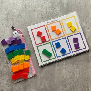 May include: A color sorting activity set featuring a workbook with color-coded squares and a mesh bag filled with matching colored tiles. The workbook has the text "Sort the tiles by color". The tiles are red, orange, yellow, green, blue, and purple.