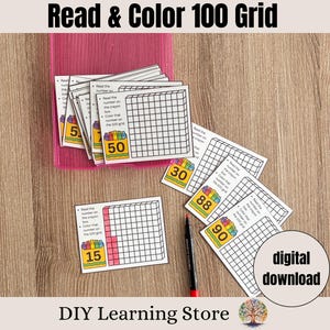 May include: A collection of printable educational cards with the text "Read & Color 100 Grid". The cards feature a grid, numbers, and instructions. A pink plastic holder contains some cards. A black and red pen is also present. The words "digital download" are visible.