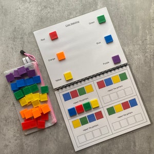 May include: A color matching activity book with a spiral binding, featuring red, orange, yellow, green, blue, and purple squares. A pink mesh bag filled with matching squares is also included. The text "Color Matching" is visible.