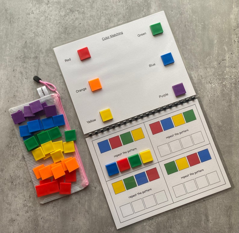 May include: A color matching activity book with a spiral binding, featuring red, orange, yellow, green, blue, and purple squares. A pink mesh bag filled with matching squares is also included. The text "Color Matching" is visible.