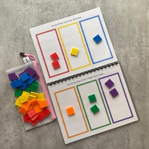May include: A color sorting activity set. The set includes a spiral-bound booklet with color sorting pages and a clear mesh bag filled with colorful square tiles. The booklet pages read "Sort the Primary Colors: Red, Yellow, Blue" and "Sort the Secondary Colors: Orange, Green, Purple."