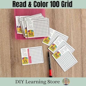 May include: Educational activity cards with the text "Read & Color 100 Grid". The cards feature a 100 grid, numbers, and instructions. A red and black marker is also present. The cards are on a wooden surface.